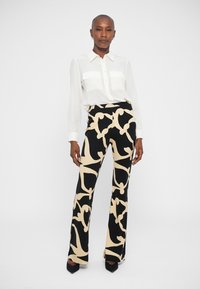 Calças de cintura alta pretas e bege com padrão, design ajustado, combinadas com uma camisa branca de colarinho. Corte slim com uma ligeira flare na parte inferior.