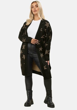 Cardigan lungo lavorato a maglia nera con motivo a leopardo, bordi a coste e apertura frontale, abbinato a pantaloni neri in ecopelle e stivali.