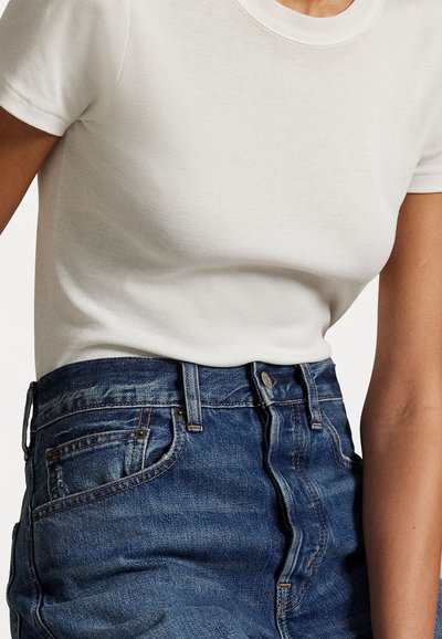 Hvit bomulls t-skjorte med korte ermer, sammen med blå denim høyt midjebukser med frontknapp og fem lommer.