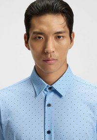 Camicia button-up azzurro chiaro con un piccolo motivo geometrico, colletto strutturato e texture liscia, con un design aderente.