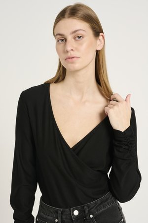 Black long-sleeve top with a deep V-neck, made of soft fabric. Features gathered detail on sleeves and paired with high-waisted jeans.