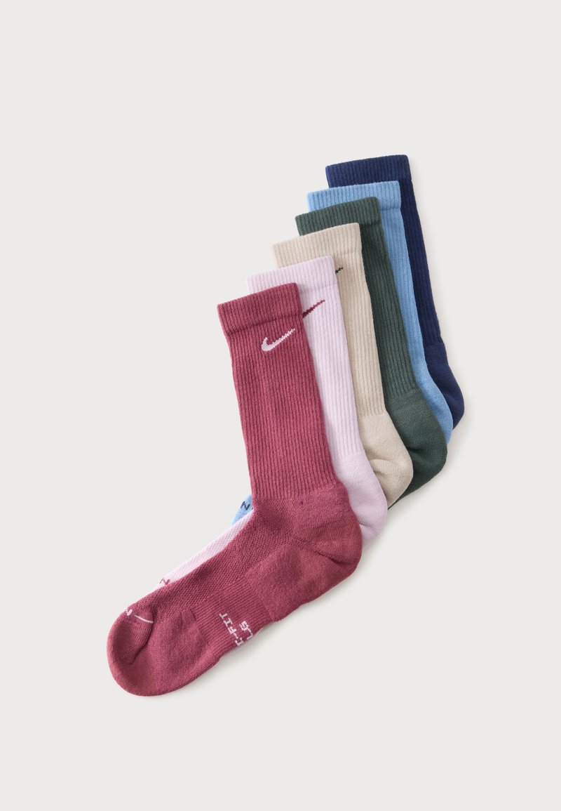 Six paires de chaussettes Nike crew en bordeaux, rose clair, beige, vert foncé, bleu clair et bleu marine, empilées soigneusement sur un fond blanc.