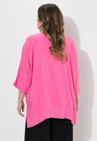 Blusa rosa over-size con maniche a 3/4, tessuto leggero, orlo rotondo e drappeggio sottile. La vista posteriore mostra una texture liscia e un design fluido.