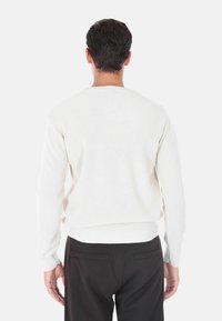 Maglione bianco a maglia con texture a coste, dotato di maniche lunghe e scollo rotondo, abbinato a pantaloni scuri.