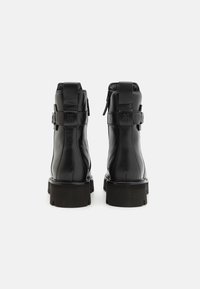 Bottines en cuir noir avec une semelle épaisse, dotées d'une fermeture éclair et d'accents de boucles décoratives sur les côtés. Texture lisse et design structuré.