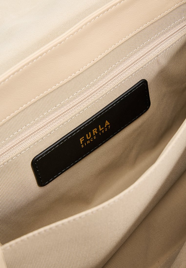 Interno della borsa beige con una texture liscia, dotato di un'etichetta in pelle nera impresso con "FURLA SINCE 1927" e tasche con cerniera.