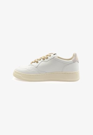 Zapatilla blanca de cuero con cordones beige. Presenta una puntera perforada, líneas de diseño sutiles y un acento texturizado en el talón. Suela de goma.