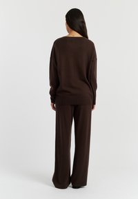 Bruin gebreid sweater en bijpassende wijde broek, met een relaxte pasvorm en zachte textuur, weergegeven vanaf de achterkant tegen een witte achtergrond.