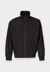 Schwarze leichte Jacke mit hohem Kragen und Reißverschluss. Mit weißen Nähakzenten an Schultern und Ärmeln. Elastische Bündchen.