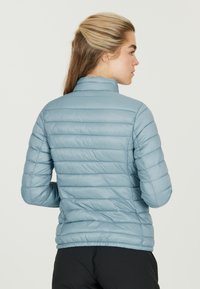 Lyseblå dunjakke med lodret quiltning, høj krave og lange ærmer. Glat tekstur og letvægtsdesign.