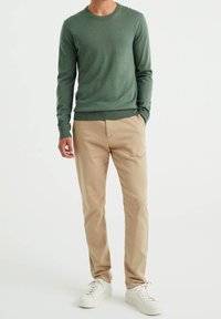 Grön stickad tröja med rund hals, kombinerad med beige byxor med raka ben och vita sneakers, som visar en avslappnad outfit.