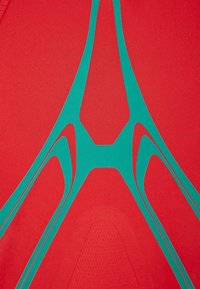 Tela deportiva roja con una textura suave que presenta diseños y acentos geométricos en color verde azulado, creando un contraste visual dinámico.