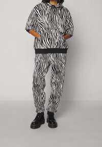 Sudadera a rayas de cebra en blanco y negro con un bolsillo frontal, combinada con pantalones a juego. Presenta un corte holgado y puños elásticos, usada con botas negras.