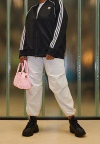 Mustat vetoketjulliset takit, joissa on valkoiset raidat, valkoiset väljät housut, mustat paksut lenkkikengät ja pieni vaaleanpunainen käsilaukku. Sileät ja kiiltävät pinnat.