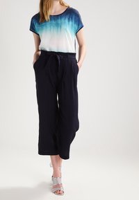 Top de manga corta con degradado en azul y blanco, combinado con culottes de talle alto en azul marino y sandalias plateadas con tiras. Tejido suave, corte relajado.