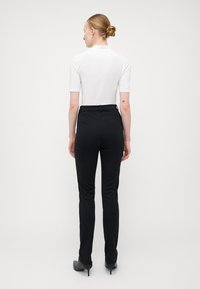 Sorte skreddersydde bukser med slim fit og glatt tekstur, kombinert med en ensfarget hvit kortermet topp, sett bakfra.