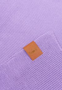 Dzianina w kolorze fioletowym z teksturowanym wzorem; posiada brązową skórzaną metkę wytłoczoną z wzorem.