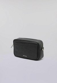 Svart rektangulär väska i slätt läder med en strukturerad frampanel, silverfärgad dragkedja och subtil branding på den nedre framsidan.