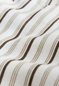 Tissu blanc à rayures verticales marron et beige, montrant la texture et des plis délicats.