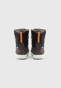 Un par de zapatillas altas en negro y gris con tiradores naranjas, vistas desde atrás sobre un fondo blanco.