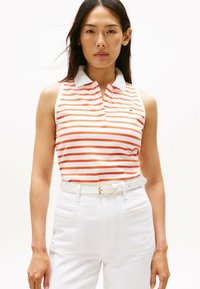 Pasek w paski bez rękawów w kolorze pomarańczowym i białym; ma klasyczny kołnierzyk oraz małe logo na piersi; w komplecie z białymi spodniami z paskiem.