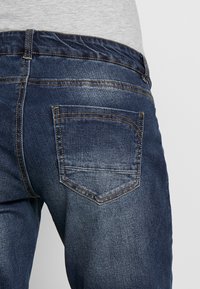 Jeans i mörkblått denim med en flexibel midja, bakficka med en svängd söm och ljus blekning längs låren och sätesområdet.