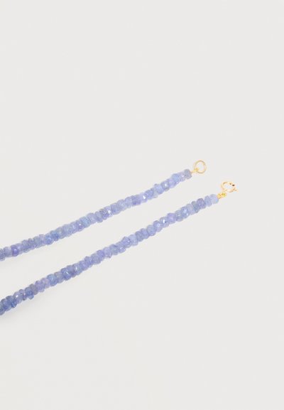 Στεφάνι από διαμορφωμένες ανοιχτό μοβ-μπλε χάντρες με μικρά χρυσά κούμπωματα σε κάθε άκρη σε λευκό φόντο.