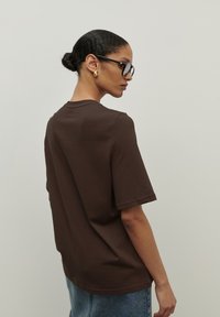 Brązowa bawełniana oversize'owa koszulka z krótkim rękawem, okrągłym dekoltem i minimalistycznym designem. Charakteryzuje się gładką fakturą bez wzorów.