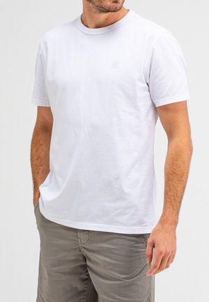 White cotton T-shirt with a crew neckline and short sleeves. Features a subtle logo on the chest and a relaxed fit. Worn with gray trousers.