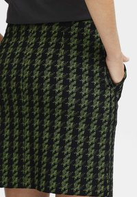 Zwarte rok met een gestructureerd houndstoothpatroon in groen. Kenmerkt zich door zijzakken en een getailleerd ontwerp, met een midi-lengte.