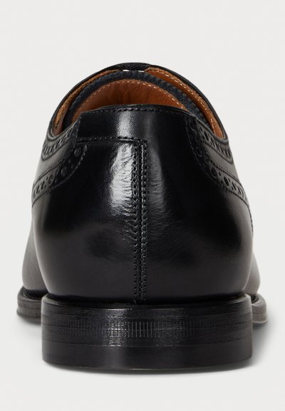 Scarpe eleganti in pelle nera con dettagli brogue, texture liscia, punta rotonda e tacco basso con suola texture.
