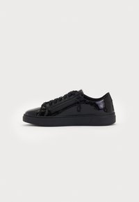Madala musta patendi nahast paari sneakerid mustade kotaotega, kummist tallaga ja külgmise lukuga detailiga heledal taustal.
