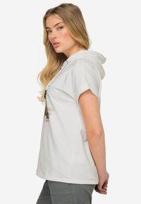 Sudadera blanca de manga corta con un estampado gráfico en la parte frontal, cuello con cordón y corte relajado. Material de algodón suave, diseño casual.