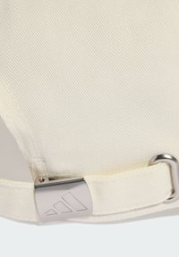 Gorra de algodón blanca con tejido texturizado, que presenta un clip de ajuste de metal plateado y un detalle de logo de marca. Diseño limpio y minimalista.