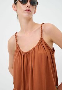 Top marrone senza maniche con scollatura arricciata e spalline intrecciate, realizzato in tessuto morbido, con un fit rilassato e una caduta morbida.
