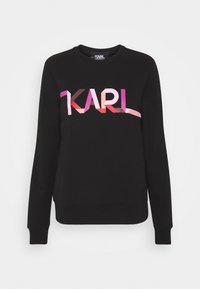 Sudadera negra con cuello redondo. En la parte frontal presenta un logotipo degradado "KARL" en tonos de rosa y rojo. Puños y dobladillo acanalados. Textura de tela suave.