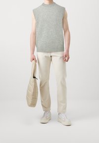Pull sans manches gris clair en maille, ourlet côtelé, associé à un pantalon crème et un sac matelassé beige. Baskets blanches avec des accents pastel.