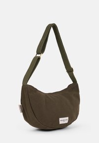 Olive green canvas shoulder bag with a curved shape, featuring a woven strap and a label detailing the brand at the side.