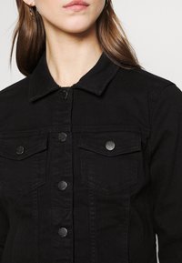 Mustaparran takki, jossa on kauluskenttä, hopeiset napit, kaksi rintataskua ja teksturoitu pinta.