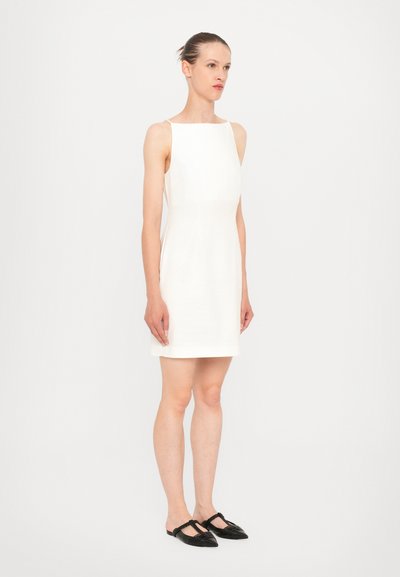 Hvid ærmeløs kjole med bådudskæring, lige pasform og minimalistisk design. Sorte slip-on sko med struktureret detaljer og spidse tå.