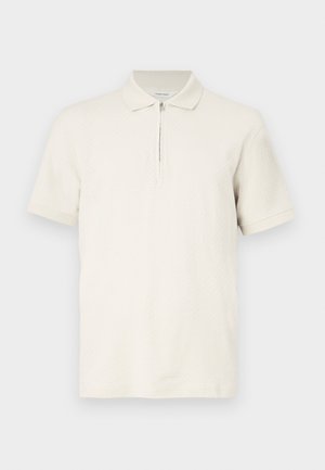 Kortärmad polo i ljus krämfärg, tillverkad av strukturerat tyg, med halvlång dragkedja och klassisk krage. Slät, avslappnad design.