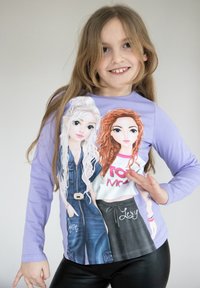 Maglietta a maniche lunghe viola con personaggi illustrati dai capelli biondi e rossi, vestiti con abiti casual. Il testo recita "Giugno" e "Lexy."