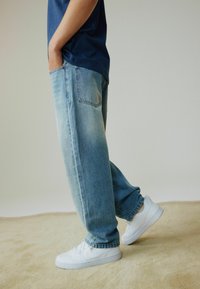 Lyseblå denimjeans med løs pasform, der har to baglommer og en let falmet tekstur. Kombineret med hvide sneakers.