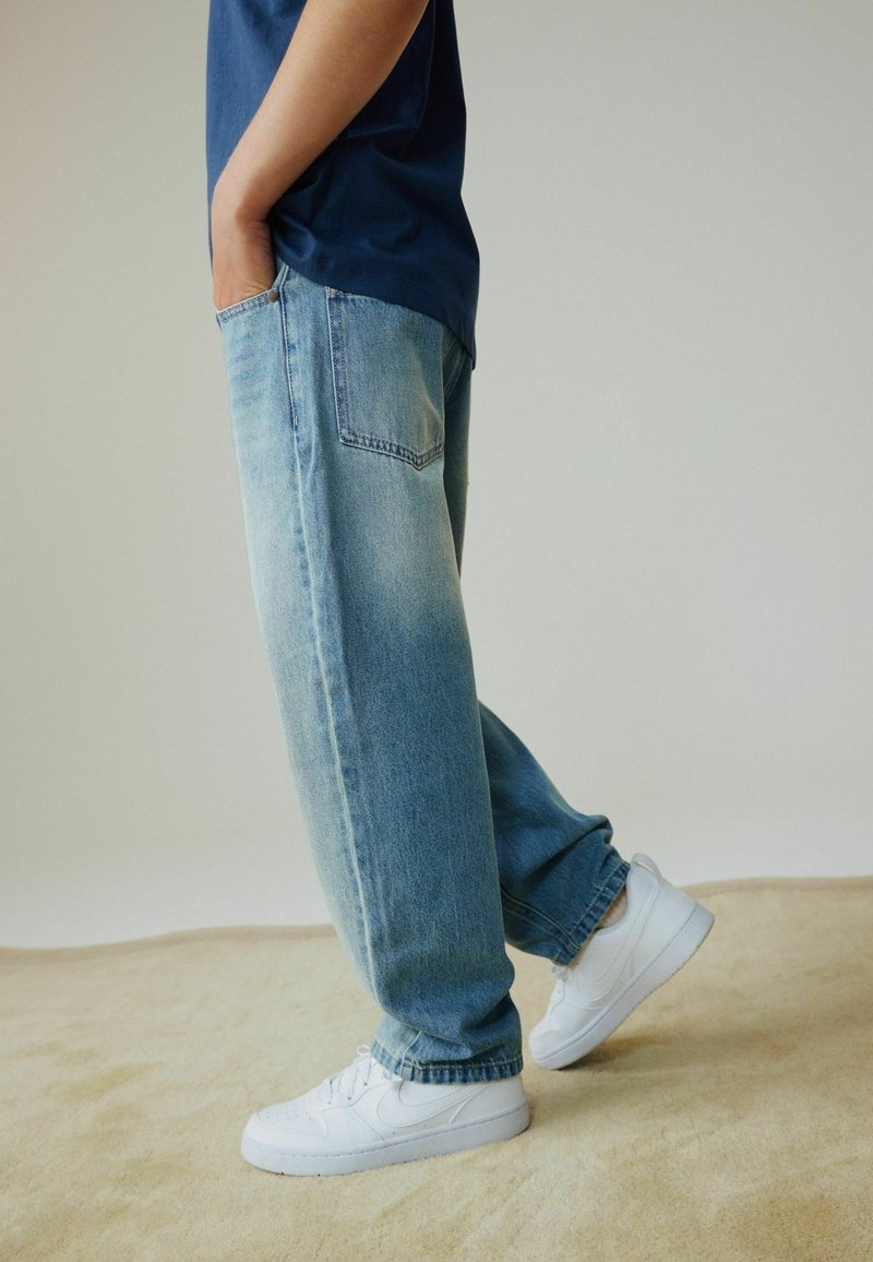 Vaaleansiniset rentoistuvaiset farkut, joissa on kaksi takataskua ja hieman haalistunut pinta. Yhdistetty valkoisiin tennareihin.