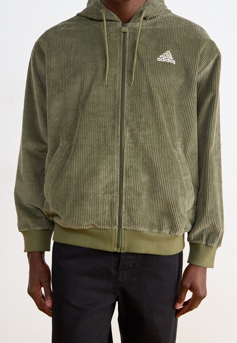 Olivgrön corduroy hoodie med dragkedja, ribbade mudd och nederkant, kengurufickor och vitt Adidas-logga på vänster bröst.