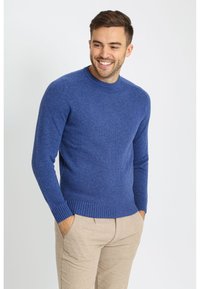 Blauwe gebreide trui met een geribbelde zoom en manchetten. Ronde halslijn. Gecombineerd met lichtbeige broek met een losse pasvorm en zakken.