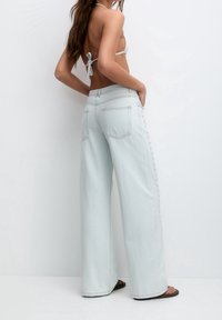 Jean large bleu clair en denim, doté d'une taille haute, d'accents de boutons latéraux et de poches arrière. Design minimaliste avec une finition propre.