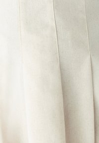 Pleated, off-white fabric with a textured, natural finish. The material appears soft with subtle specks, enhancing its organic look.