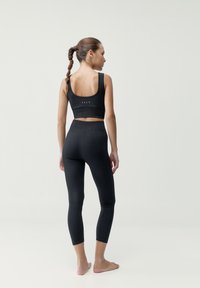 Čierny rebrovaný športový top a legíny s priliehavým strihom. Top má široké ramienka a decentné logo; legíny s dĺžkou po členky.