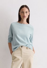 Hellblauer Rundhalsausschnitt-Pullover aus weichem Stoff mit langen Ärmeln, kombiniert mit beigen, gestreiften Cordhosen mit Knopfverschluss.